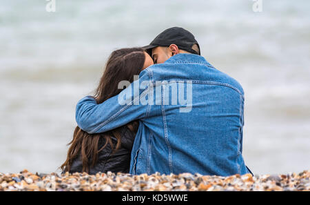 Junges Paar sitzt auf einem Strand küssen und umarmen einander. Junge Geliebte umarmen am Strand. Stockfoto