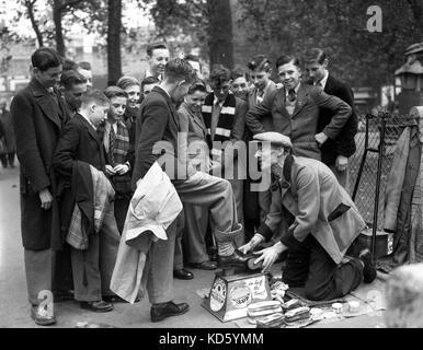 Deaktiviert Schuhputzmaschine/-Mann mit nur einem Bein polieren school Jungen Schuhe auf in London 1954 Schuhputzmaschine/-mann. Stockfoto