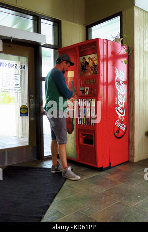 Ein Mann Geld in einem roten coca cola Maschine in einer Ruhezone. Stockfoto