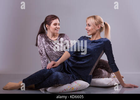 Zwei Frauen in den Schlafanzügen sitzen auf Kissen auf einem grauen Hintergrund. Studio shoot Stockfoto