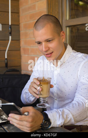 Porträt eines gutaussehenden und positiven jungen Mannes, der in einem Café sitzt und Kaffee trinkt Stockfoto