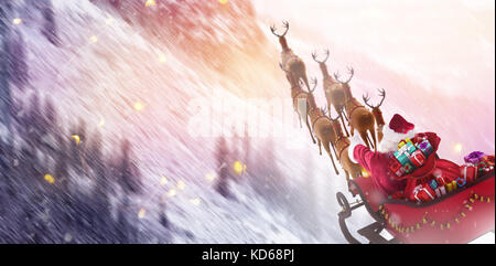 Hohe Betrachtungswinkel von Santa Claus reiten auf Schlitten mit Geschenkbox gegen verschneite Pinien auf der Alp Berghang Stockfoto