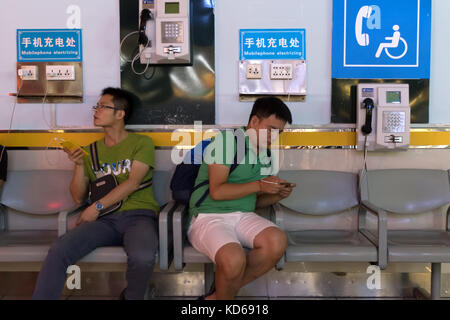 Chinesen und Touristen mit Telefonen am Liangjiang International Airport in Guilin, China, Asien. Passagiere, die unterwegs Smartphones aufladen Stockfoto