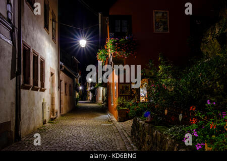 Eine kleine beleuchtete Straße führt durch die Blume dekoriert Fachwerkhäuser der historischen Altstadt bei Nacht Stockfoto