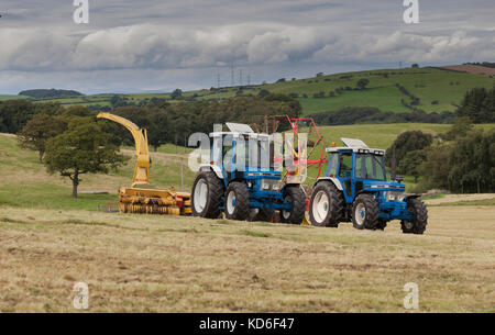 2 vintage Ford Traktoren; 1991 Ford 7810, Generation 3, auf Pottinger 771a Rake. 1988 Ford 7610, tritt zwei, - auf New Holland Feldhäcksler. Stockfoto