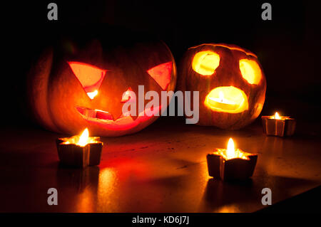 Scary Halloween Kürbis und Melone Jack-o-lanterns auf schwarzen Hintergrund mit kleinen, runden und Star Kerzen. selektive Fokus, Bokeh. Stockfoto