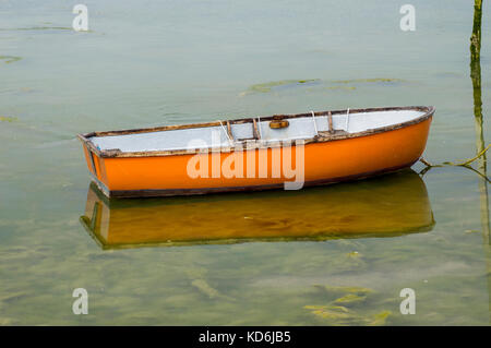 Orange Holzboot auf ruhigem Wasser bei Ebbe vertäut. Stockfoto