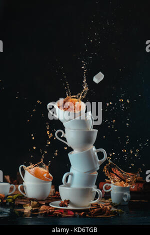 Stapel weiße Kaffeetassen mit dynamischen Spritzer und Tropfen auf einem dunklen Hintergrund. Küche durcheinander und Mad Tea time Konzept. Aktion essen Fotografie Stockfoto