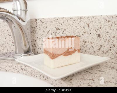 Natürliche Handarbeit Beauty Bar soap auf einer weißen Platte durch das Bad Armatur. Rosa pflanzliche Seife mit rosa Ton, ätherische Öle, und Olivenöl. Stockfoto