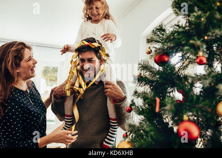 Glückliches junges Paar mit ihrer Tochter Weihnachten feiern. Kleines Mädchen sitzen auf den Schultern ihres Vaters und Spaß haben. Stockfoto