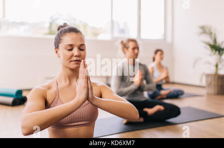 Junge Frau mit Yoga in der Turnhalle Klasse im Fitnesscenter mit Menschen im Hintergrund. Menschen meditieren im Health Club. Stockfoto