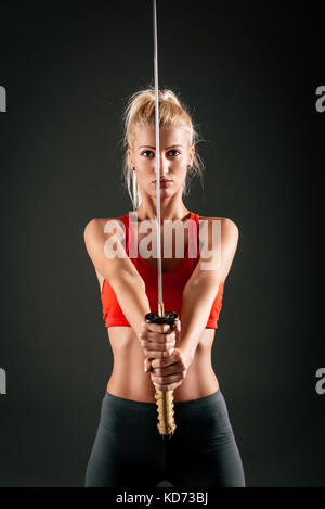 Süße blonde Mädchen mit einem ernsten Ausdruck auf ihrem Gesicht mit einem Katana mit ausgestreckten Händen und Blick in die Kamera. Stockfoto