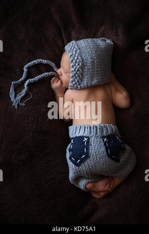 Neugeborenes Baby in einem grauen gestrickten Anzug schläft in einem schönen darstellen Stockfoto