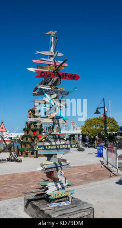 Wegweiser von Key West bis Reiseziele mit Pfeilen und Kilometerstand mit Weihnachten Lobster Pot Baum im Hintergrund. Stockfoto