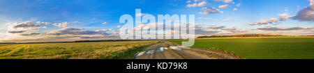 Schönen ländlichen Herbst Landschaft Panorama mit Strasse, Feld und blauer Himmel mit weißen Wolken. Panoramablick Herbst anzeigen. Sonnenuntergang über landwirtschaftliche Felder und Stockfoto