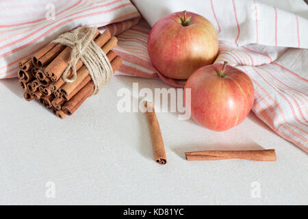 Frische reife rote Äpfel und Zimtstangen auf weißem Holz- Hintergrund. Stockfoto