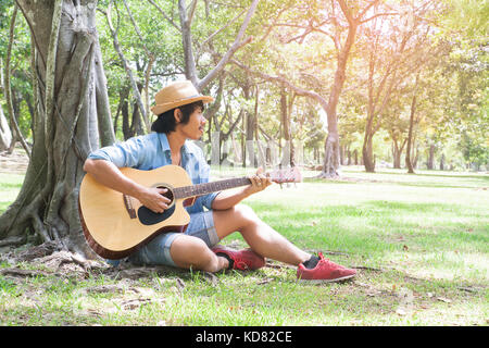 Stattliche Asiaten Gitarre spielen im Park, Lifestyle im Sommer, glückliche Menschen Stockfoto