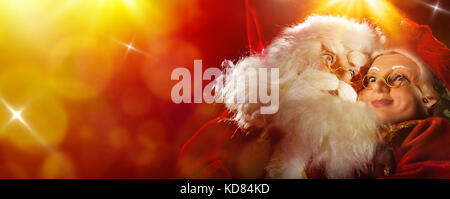 Santa Claus und Frau Claus festhalten zu den roten und gelben Hintergrund mit Lichtern und glänzt. Stockfoto