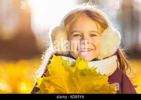 Happy kleines Mädchen in ohrenschützern mit Blätter im Herbst Stockfoto