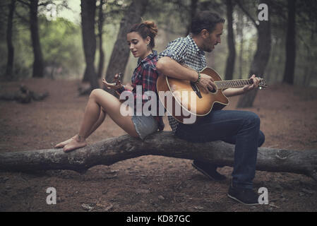 Mann und Mädchen sitzen im Wald und spielen Gitarre und Ukulele, Spanien Stockfoto