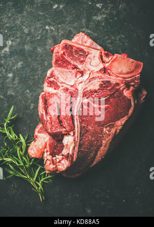 In der Nähe des frischen, rohen ungekochten Rindfleisch T-Bone Steaks mit Rosmarin über schwarzen Stein Stapel abgelegt, selektiver Fokus, kopieren Raum Stockfoto