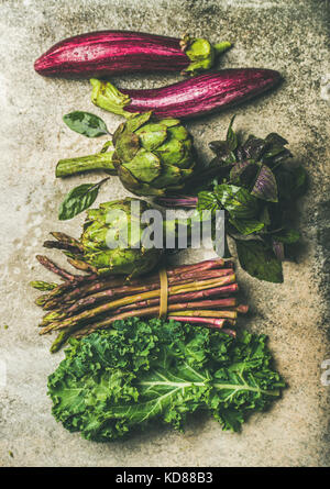 Flachbild-lay von Grün und Violett frisches Gemüse Vielfalt über konkreten Hintergrund, Ansicht von oben. Lokalen, saisonalen Produkten für gesundes Kochen. Eggplans, Bohnen, Stockfoto