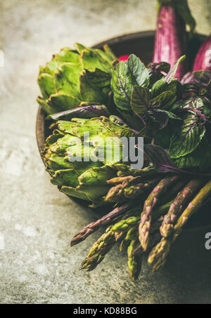 Grün und lila Gemüse auf der Platte über grauer Hintergrund, selektiven Fokus. Lokale Produkte für gesundes Kochen. Eggplans, Bohnen, Kohl, Spargel, Artic Stockfoto