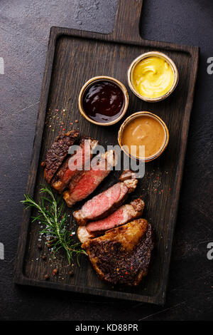 In Scheiben geschnitten Gegrilltes Rib Eye Steak und drei verschiedenen Saucen: Pepper Sauce, Senf und Grill auf dunklem Hintergrund Stockfoto