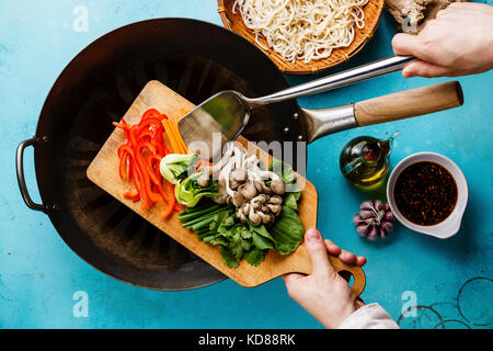 Kochvorgang Udon Nudeln mit Austernpilzen und Gemüse und männlichen Hand auf blauem Hintergrund Stockfoto
