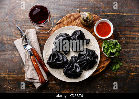 Schwarz georgischen Knödel Khinkali mit Fleisch und Tomaten würziger Soße auf weiße Platte und Wein Stockfoto