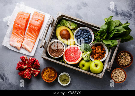 Gesunde Lebensmittel sauber essen Auswahl im Holzkasten: Fisch, Obst, Gemüse, Samen, superfood, Getreide, Blattgemüse auf grauem Beton Hintergrund Stockfoto