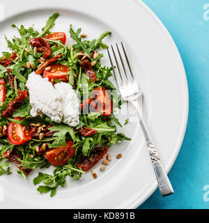 Salat mit Rucola, getrocknete Tomaten, Sonnenblumenkerne und Ricotta auf weiße Platte close-up Stockfoto