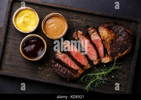 In Scheiben geschnitten Gegrilltes Rib Eye Steak und drei verschiedenen Saucen: Pepper Sauce, Senf und Grill auf dunklem Hintergrund Nahaufnahme Stockfoto