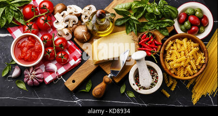 Italienische Lebensmittelzutaten mit Oliven, Pasta Spaghetti, Olivenöl, Parmesan, braune Pilze, Tomaten, Knoblauch, Basilikum, Chili, Pfeffer und Gewürze auf dunklen m Stockfoto