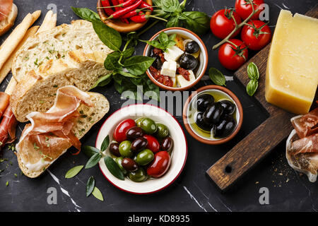 Italienische Snacks essen mit Schinken, geschnittenem Brot Ciabatta, Oliven, Feta Käse mit getrockneten Tomaten und Parmesan auf dunklem Marmor Hintergrund Stockfoto