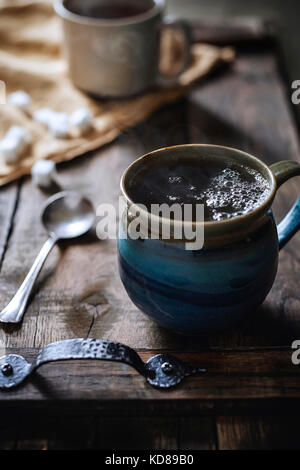 Handgefertigte Stein Tasse dampfenden Tee auf rustikalem Holz Tablett serviert mit morgen Licht dahinter. Stockfoto