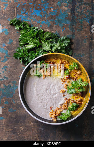 Pilz Cremesuppe in Schwarz Keramik Schüssel mit kurkuma Pulver, Wald, Pilzen, grüne Petersilie, gebratenen Zwiebeln über alten dunklen Hintergrund. Stockfoto