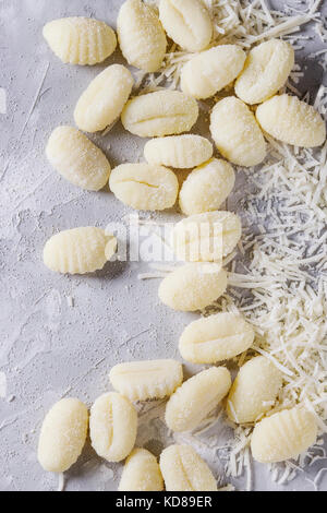 Rohen ungekochten Kartoffel Gnocchi mit Mehl und geriebenen Parmesan über grauer Beton Hintergrund. Ansicht von oben, aus der Nähe. Home Kochen. Stockfoto