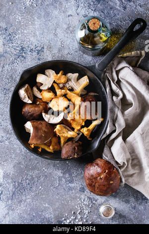 Haufen frischer Wald Steinpilze Steinpilze und Pfifferlinge Pilze in Gusseisen Pfanne mit Olivenöl und Salz, serviert textile Serviette mit Messer über gr gewonnen Stockfoto