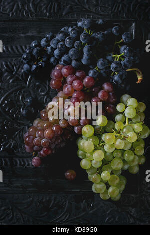 Vielzahl von drei Art frische reife Trauben dunkel Blau, Rot und Grün. Close up über Black Metal verzierten Hintergrund. Ansicht von oben Stockfoto