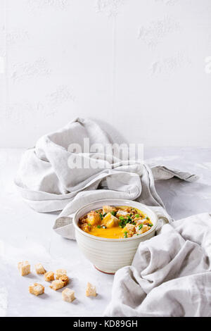 Becher vegetarische Kürbis Karotten Suppe mit Croutons und Zwiebeln auf Textil Serviette über Grau Weiß konkreten Hintergrund serviert. Stockfoto