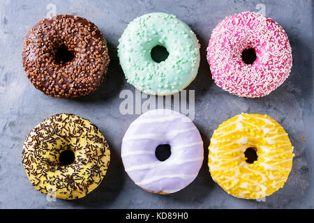 Vielzahl von Bunt glasierter Krapfen über graues Metall Textur Hintergrund. Ansicht von oben Stockfoto