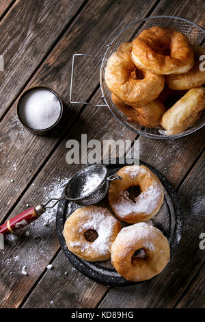 Hausgemachten Krapfen mit Zucker Pulver am Schwarzen Brett und in den Frittierkorb mit Vintage Sieb auf alten Holzbrett serviert. Im rustikalen Stil. Nach oben V Stockfoto