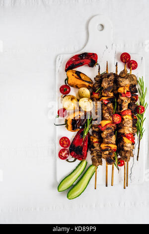 Lamm Shish Kebab serviert mit gegrillte Paprika, Schalotten, frischen Tomaten und Gurke auf einem weißen Marmor von der Ansicht von oben fotografiert. Stockfoto