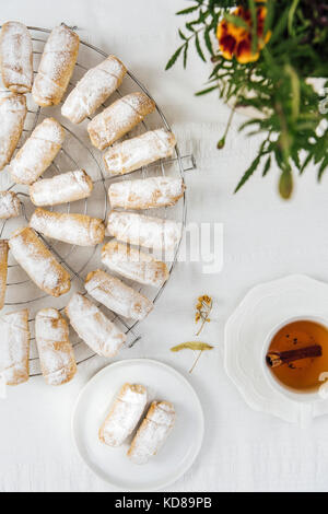 Türkische cookies gefüllt mit Apfel und Zimt auf eine Kühlung Rack auf einem weißen Hintergrund aus Sicht von oben fotografiert. Eine Tasse Tee, eine kleine Platte mit c Stockfoto
