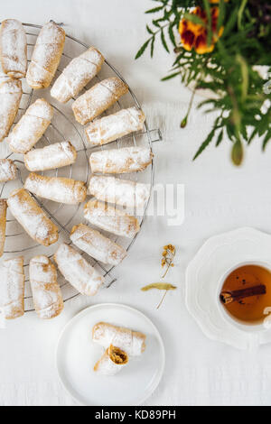 Türkische cookies gefüllt mit Apfel und Zimt auf eine Kühlung Rack auf einem weißen Hintergrund aus Sicht von oben fotografiert. Eine Tasse Tee, eine kleine Platte mit c Stockfoto