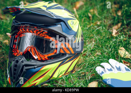 Motorrad Helm mit Handschuhe und Schutzbrille auf trockenem Laub über greem Gras. Automne Stockfoto