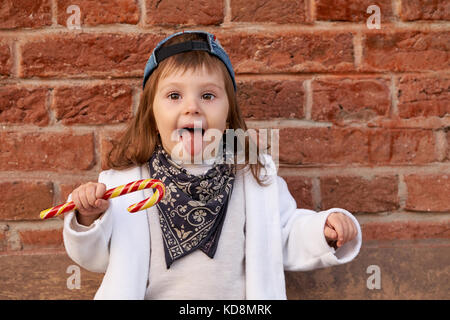 Nett schön Kind isst Süßigkeiten. Kleines Mädchen zeigt Zunge Stockfoto