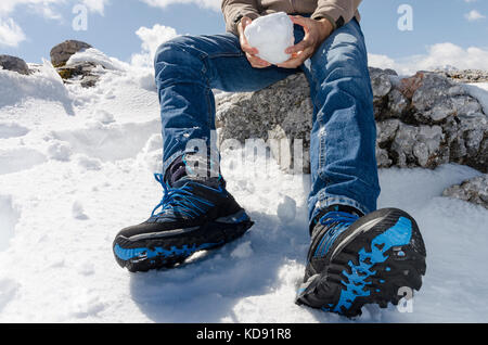 Winter Fun - ein Mann sitzt auf einem Felsen mit einem Schneeball in seine Hände in die verschneite Landschaft Stockfoto