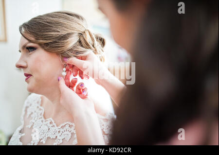Nahaufnahme einer schönen Brautjungfer helfen Braut an ihrer Hochzeit Ohrringe ins Zimmer zu stellen. Stockfoto